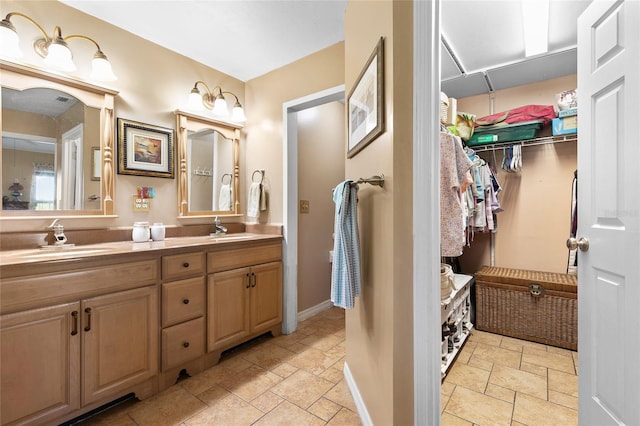 bathroom featuring a walk in closet, stone tile flooring, a sink, and double vanity