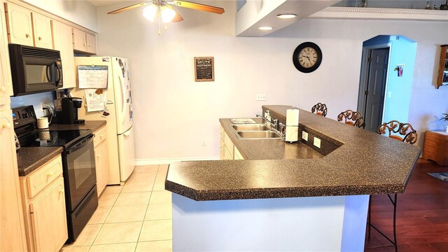 kitchen featuring a kitchen bar, a ceiling fan, black appliances, a sink, and dark countertops