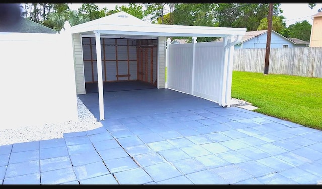 view of patio / terrace with concrete driveway, a detached garage, fence, and an outdoor structure