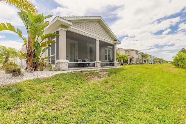 back of property featuring a sunroom, stone siding, and a lawn