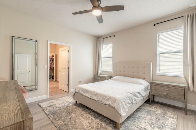 bedroom with light wood finished floors, a ceiling fan, baseboards, and a spacious closet