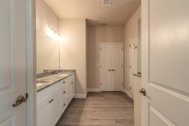 bathroom featuring wood finished floors, a sink, double vanity, baseboards, and visible vents