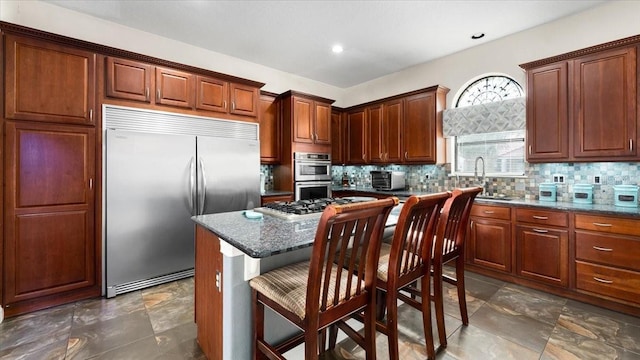 kitchen with decorative backsplash, a kitchen bar, a sink, dark stone countertops, and stainless steel appliances