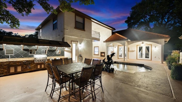 back of house featuring area for grilling, french doors, a balcony, a patio, and stucco siding