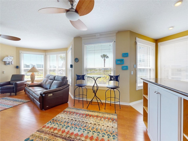 living area featuring light wood finished floors, baseboards, a textured ceiling, and ceiling fan