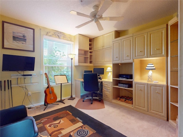 office featuring light carpet, built in desk, a textured ceiling, and ceiling fan