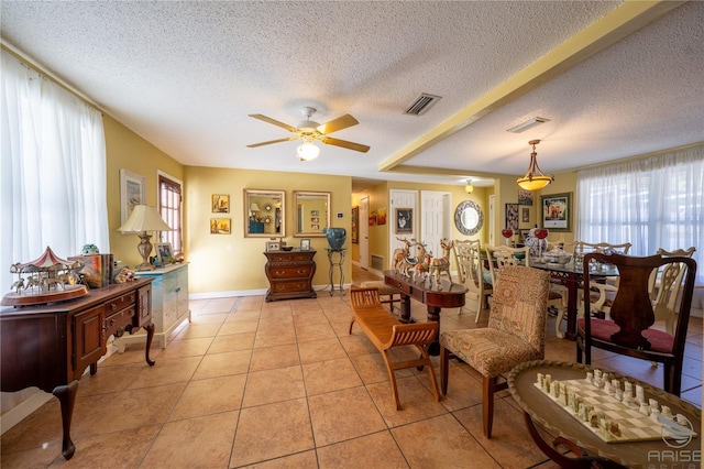 living area with ceiling fan, a wealth of natural light, a textured ceiling, and visible vents