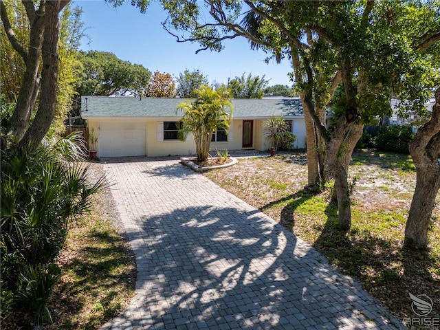 ranch-style house with a garage, stucco siding, roof with shingles, and decorative driveway