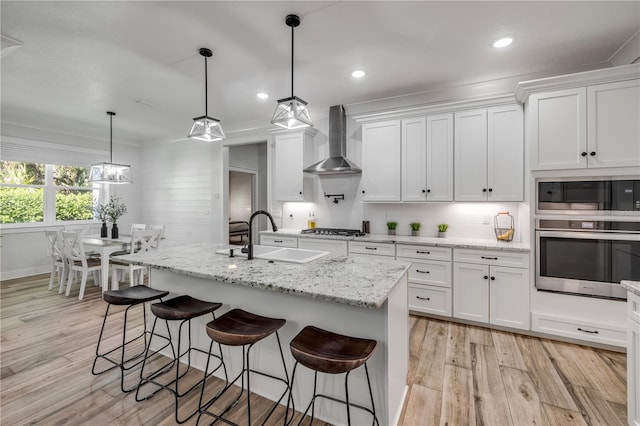 170 Live Oak Ct, New Smyrna Beach, FL 32168 - kitchen featuring wall chimney range hood, white cabinets, a sink, stainless steel appliances, and light wood finished floors
