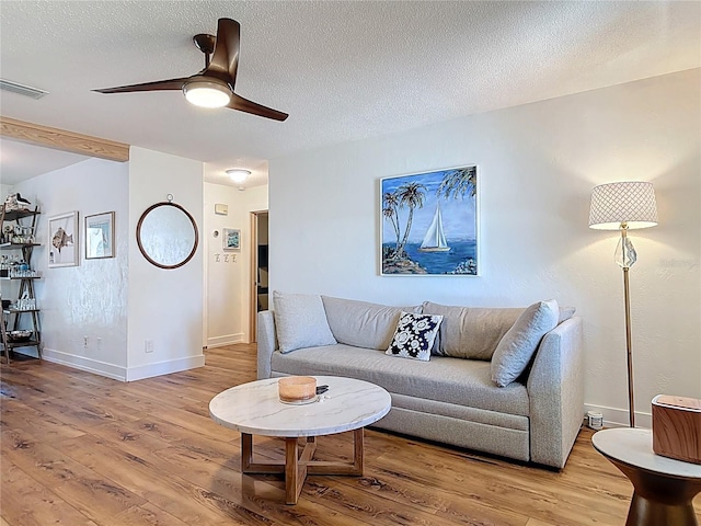 living room with a textured ceiling, a ceiling fan, visible vents, light wood finished floors, and baseboards