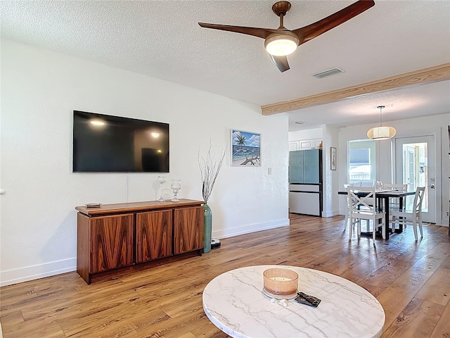 living room with light wood-style floors, ceiling fan, a textured ceiling, visible vents, and baseboards