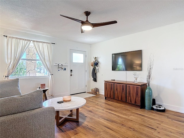 living area with a textured ceiling, a ceiling fan, baseboards, and light wood finished floors