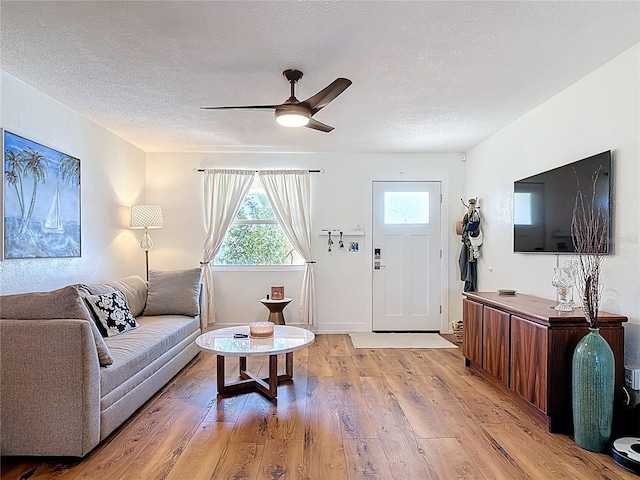 living area with a textured ceiling, ceiling fan, and light wood-type flooring
