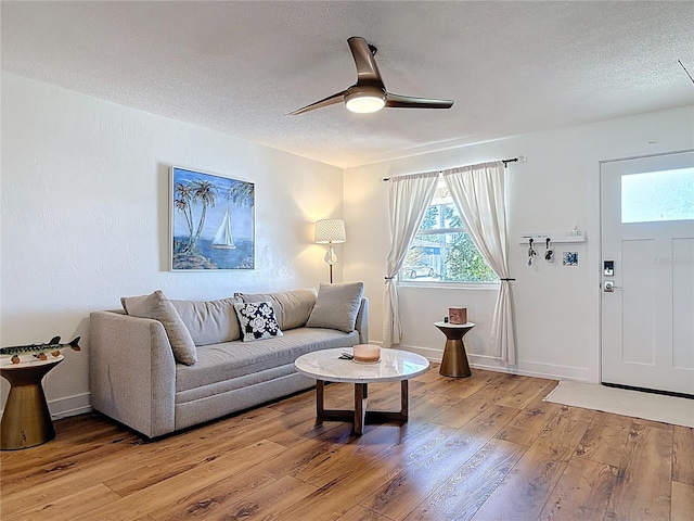 living area featuring light wood-style flooring, a textured ceiling, baseboards, and a ceiling fan