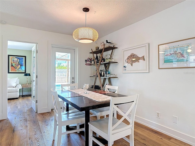 dining room with light wood-style flooring, baseboards, and a textured ceiling