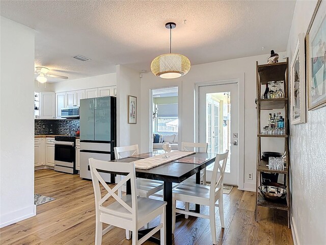 dining room with light wood finished floors, visible vents, a textured ceiling, and a ceiling fan
