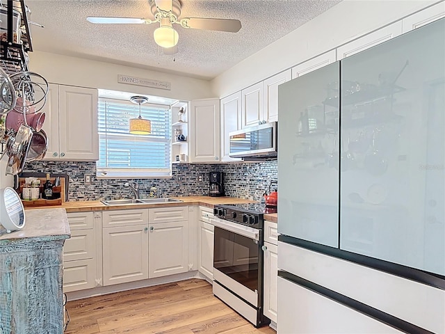 kitchen with a textured ceiling, white fridge, white cabinetry, stainless steel microwave, and range with gas stovetop
