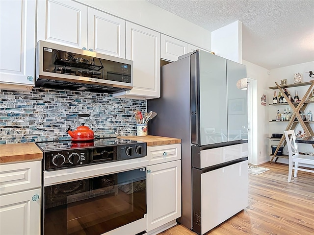 kitchen with white cabinets, freestanding refrigerator, stainless steel microwave, light wood finished floors, and butcher block countertops