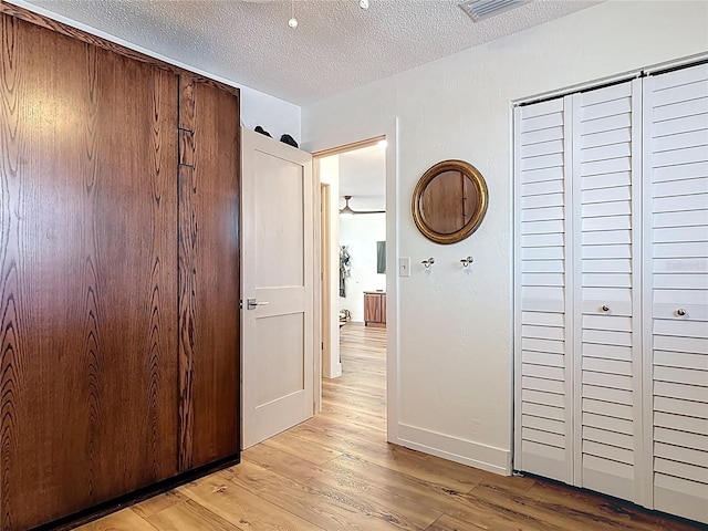 hallway featuring baseboards, light wood-style floors, a textured ceiling, and visible vents