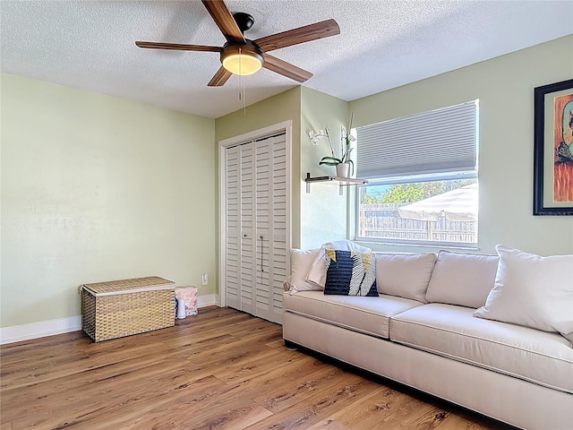 living room featuring a textured ceiling, wood finished floors, baseboards, and a ceiling fan