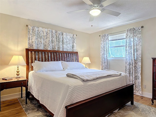 bedroom featuring a textured ceiling, wood finished floors, baseboards, and a ceiling fan