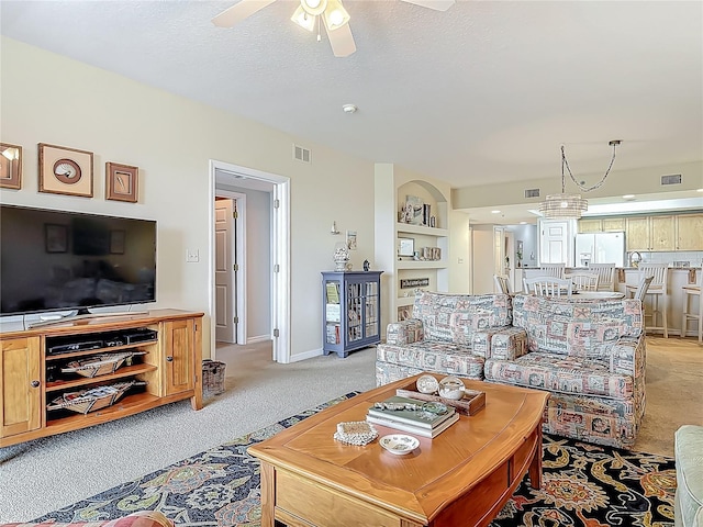 living area with a ceiling fan, visible vents, built in features, and light colored carpet