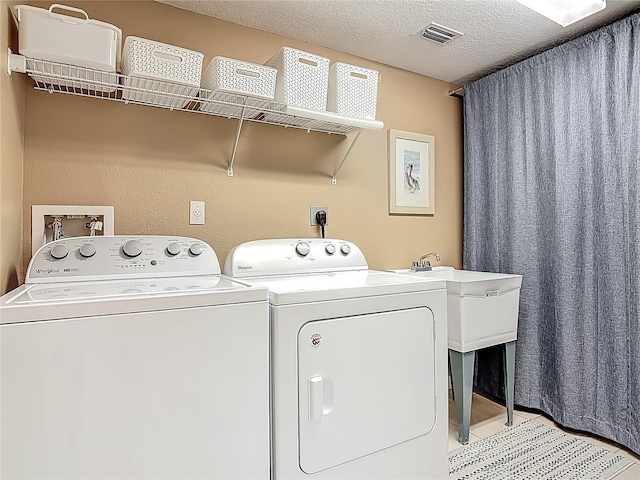 washroom with a textured ceiling, visible vents, separate washer and dryer, and laundry area