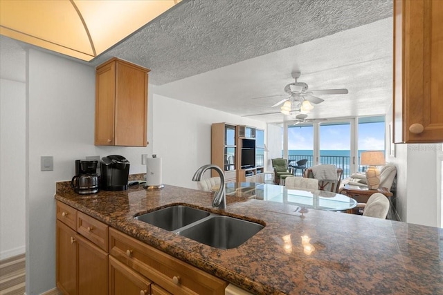 5201 S Atlantic Ave Unit 708A, New Smyrna Beach, FL 32169 - kitchen featuring a sink, ceiling fan, dark stone countertops, brown cabinetry, and a textured ceiling