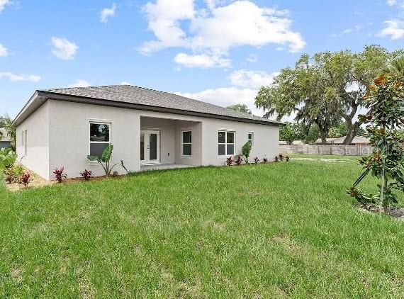 rear view of property featuring fence, a yard, and stucco siding