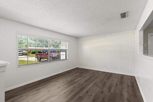 unfurnished room featuring a textured ceiling, wood finished floors, visible vents, and baseboards