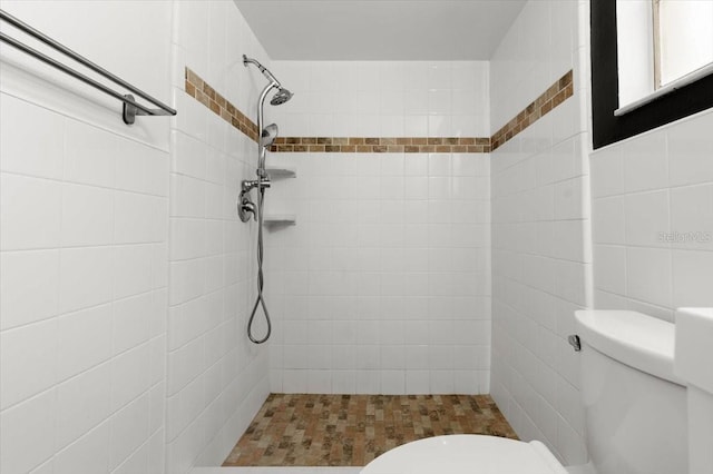 bathroom with tile walls, a tile shower, and toilet