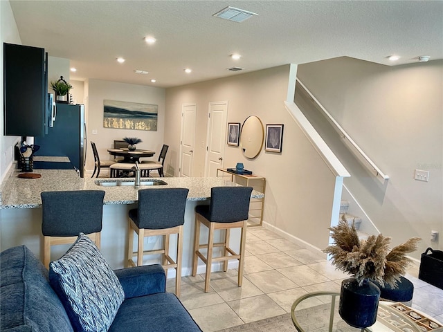 kitchen featuring a peninsula, a sink, visible vents, light stone counters, and a breakfast bar