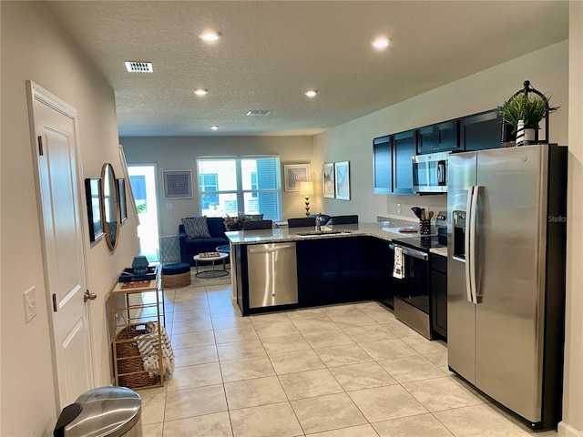 kitchen featuring a sink, open floor plan, stone counters, a peninsula, and appliances with stainless steel finishes