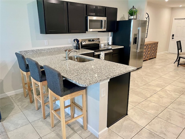 kitchen with a breakfast bar, dark cabinetry, a sink, light stone countertops, and appliances with stainless steel finishes