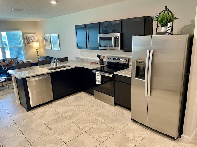 kitchen featuring a sink, light stone countertops, a peninsula, appliances with stainless steel finishes, and open floor plan