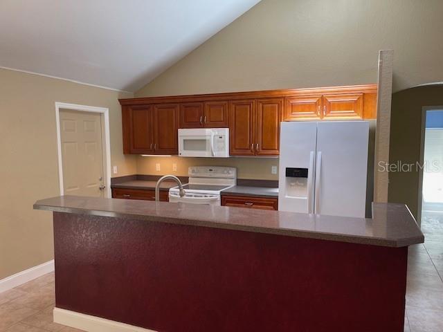 2091 Maltese Ln, New Smyrna Beach, FL 32168 - kitchen featuring brown cabinets, an island with sink, light tile patterned floors, white appliances, and baseboards
