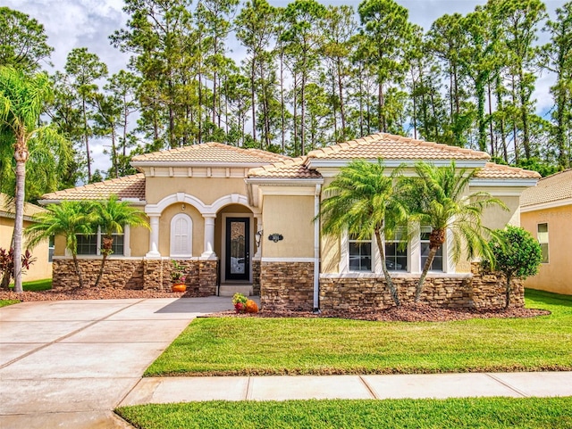 mediterranean / spanish home featuring a tiled roof, stucco siding, a front lawn, and stone siding