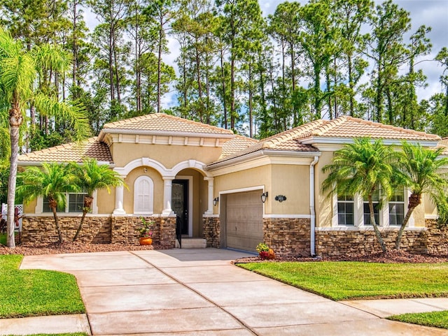 mediterranean / spanish-style home featuring concrete driveway, a tiled roof, an attached garage, and stone siding