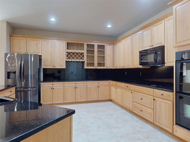 kitchen featuring light brown cabinetry, decorative backsplash, dark stone counters, and black appliances