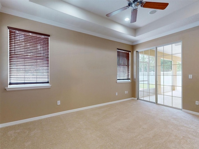 carpeted spare room featuring crown molding, a ceiling fan, a tray ceiling, and baseboards