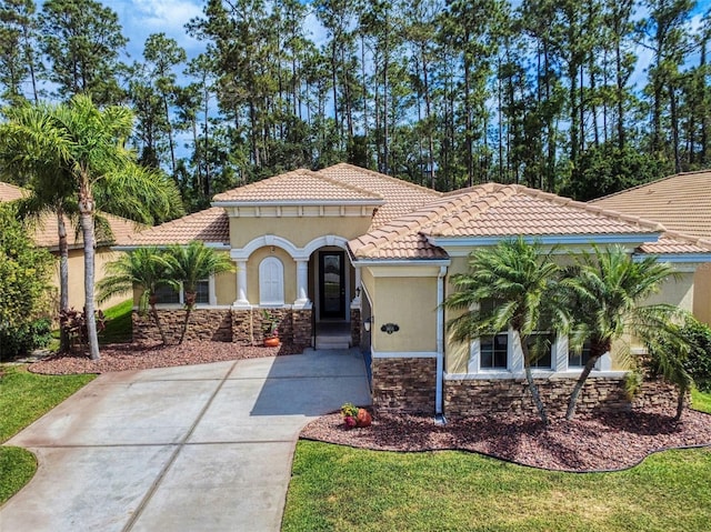 mediterranean / spanish-style home with stucco siding, concrete driveway, a tile roof, and stone siding