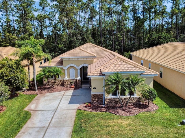 mediterranean / spanish-style house with a tile roof, stone siding, stucco siding, a front yard, and driveway