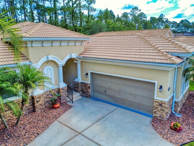 mediterranean / spanish home with a tiled roof, concrete driveway, an attached garage, stone siding, and stucco siding