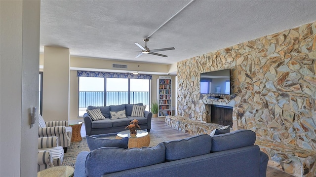 5499 Atlantic Unit 104, New Smyrna Beach, FL 32169 - living area with a ceiling fan, a textured ceiling, a stone fireplace, visible vents, and wood finished floors