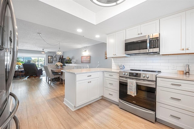 kitchen featuring light wood-style flooring, white cabinets, a peninsula, and stainless steel appliances