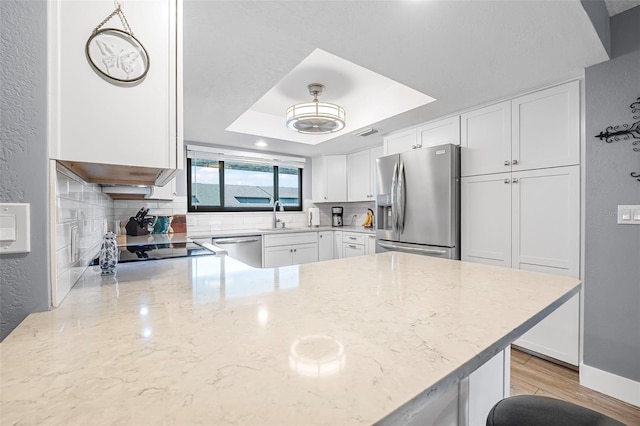 kitchen with decorative backsplash, white cabinets, a sink, appliances with stainless steel finishes, and a raised ceiling
