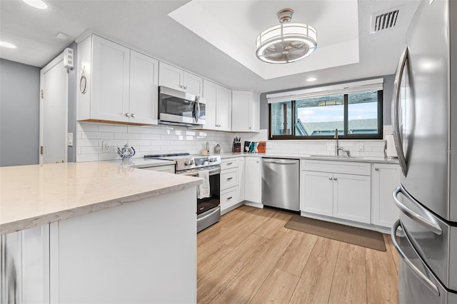 kitchen featuring light wood finished floors, stainless steel appliances, visible vents, a peninsula, and white cabinetry