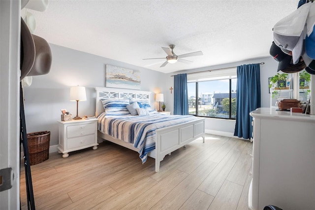 bedroom with a textured ceiling, ceiling fan, light wood finished floors, and baseboards