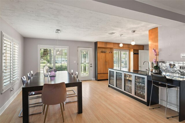 kitchen with light wood-style flooring, a sink, dark countertops, baseboards, and decorative light fixtures