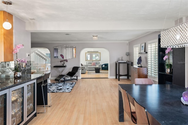 dining space with beverage cooler, visible vents, hardwood / wood-style floors, arched walkways, and ornamental molding